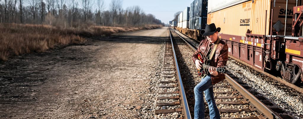 Bo Adams playing guitar by the train tracks