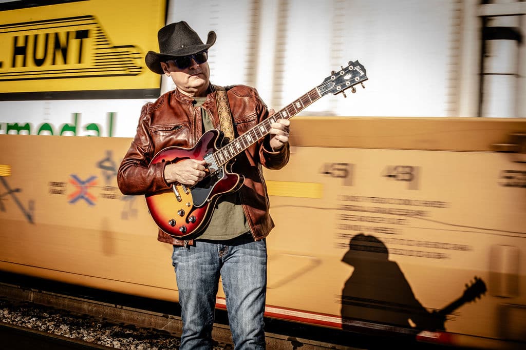 Bo Adams playing electric guitar in front of a passing freight train